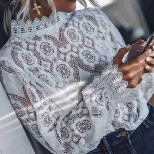 Close-up of a person wearing a white lace floral blouse with a cross earring, holding a smartphone.