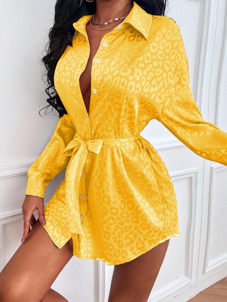 1a4b4b6b-9ecf-4807-9e5c-e747ad8508ccjpg • Punkin's Patch Bright yellow satin leopard-print shirt dress with a waist tie and button-down front, worn by a model in a posed stance.