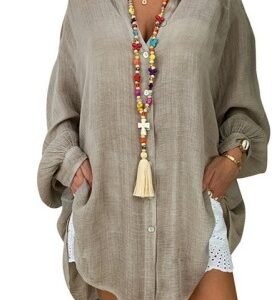 Person wearing a loose beige linen shirt dress with rolled cuffs, hands in pockets, accessorized with colorful beaded necklaces and a tassel pendant.