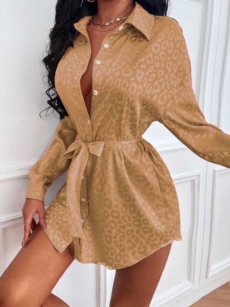 3662cb5c-001d-4c10-85b9-e081a819795ajpg • Punkin's Patch Tan leopard-print button-down shirt dress with a waist-tie belt, long sleeves, and a plunging neckline worn by a woman against a white wall.