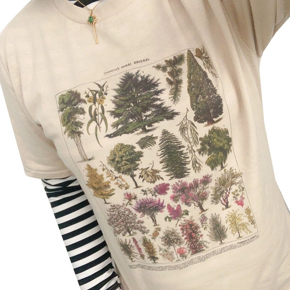 6a5625ba-241c-488b-af09-25a676a38446jpg • Punkin's Patch Beige t-shirt with a botanical print showing various trees and plants, worn over a striped long sleeve.