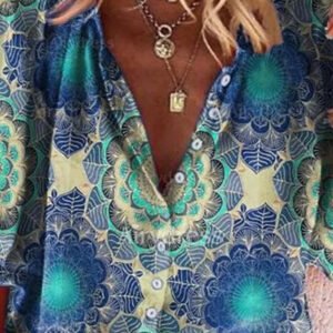 Close-up of a woman wearing a vibrant teal, blue, and yellow patterned button-down shirt with a deep V-neck and layered necklaces.