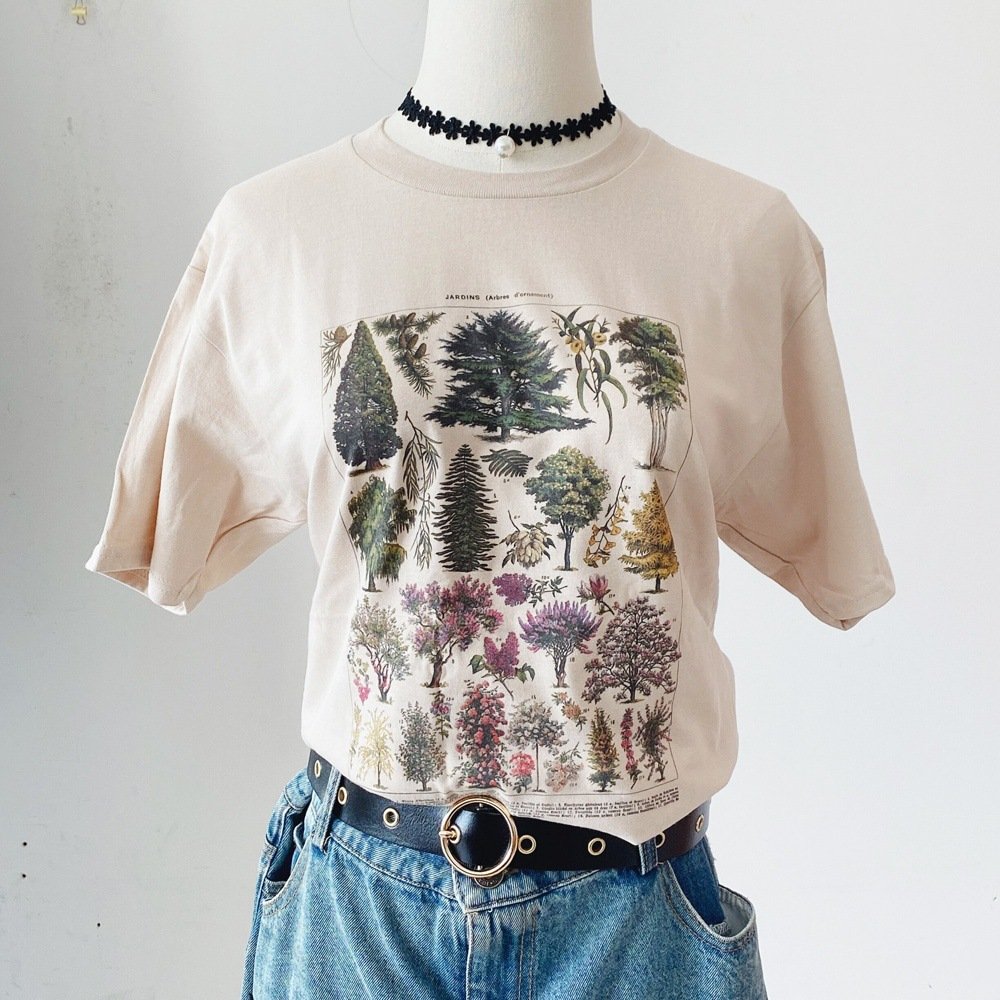b446028a-2a76-4cbf-a25e-1954f546b85djpg • Punkin's Patch Beige T-shirt on a mannequin featuring a large botanical tree print, styled with a black flower choker and blue jeans with a belt.