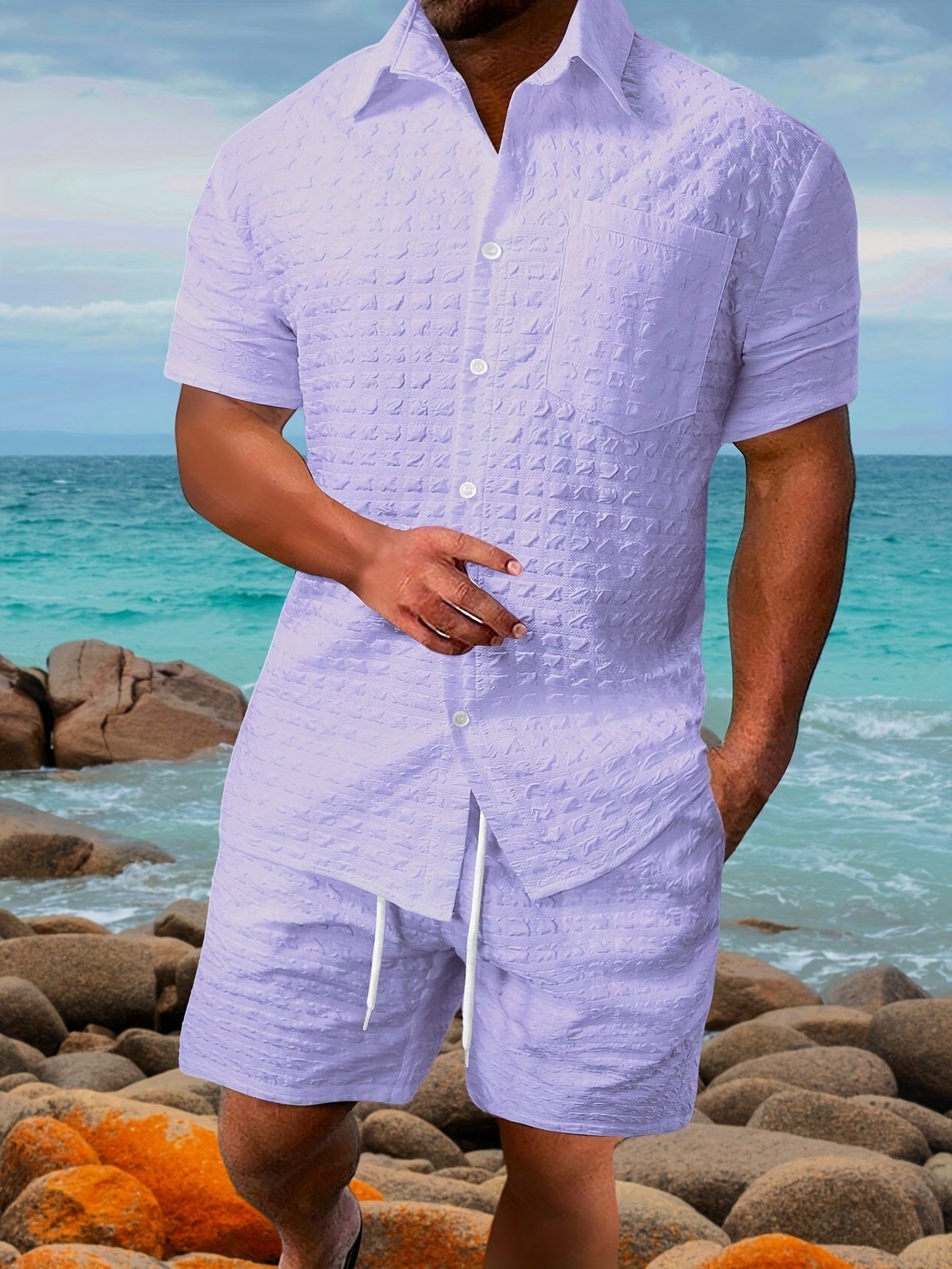 bb666cb6-22af-40a7-9363-52849f6344cdjpg ⢠Punkin's Patch Man standing on a rocky beach wearing a lavender textured short-sleeve shirt and matching shorts, with the sea in the background.
