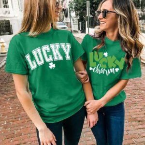 Two women wearing green T-shirts with 'LUCKY' and 'lucky charm' slogans, smiling and linked arms on a brick sidewalk.