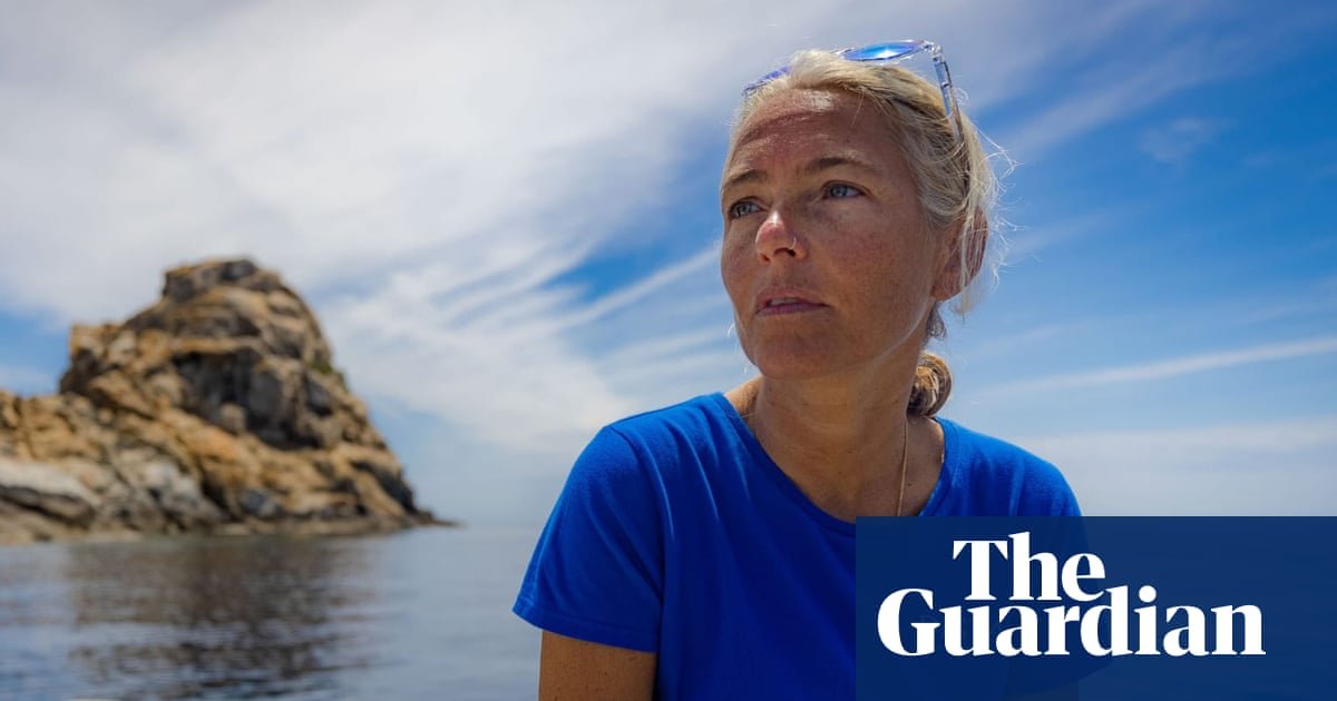 Portrait of a woman in a blue shirt looking off to the right by calm sea, with a rocky island in the background and The Guardian logo in the bottom right.