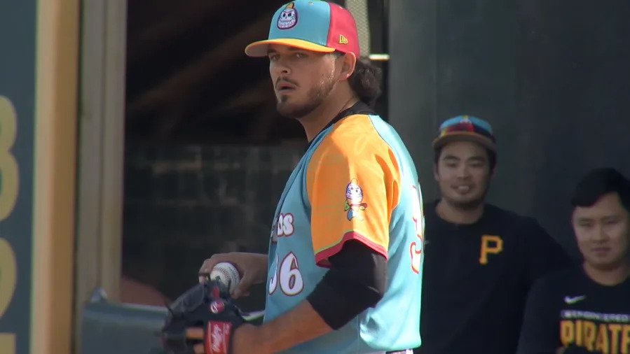 wp-header-logo-667png • Punkin's Patch Baseball player in a turquoise-orange uniform and colorful cap, holding a glove, looking to the side with teammates in the background.