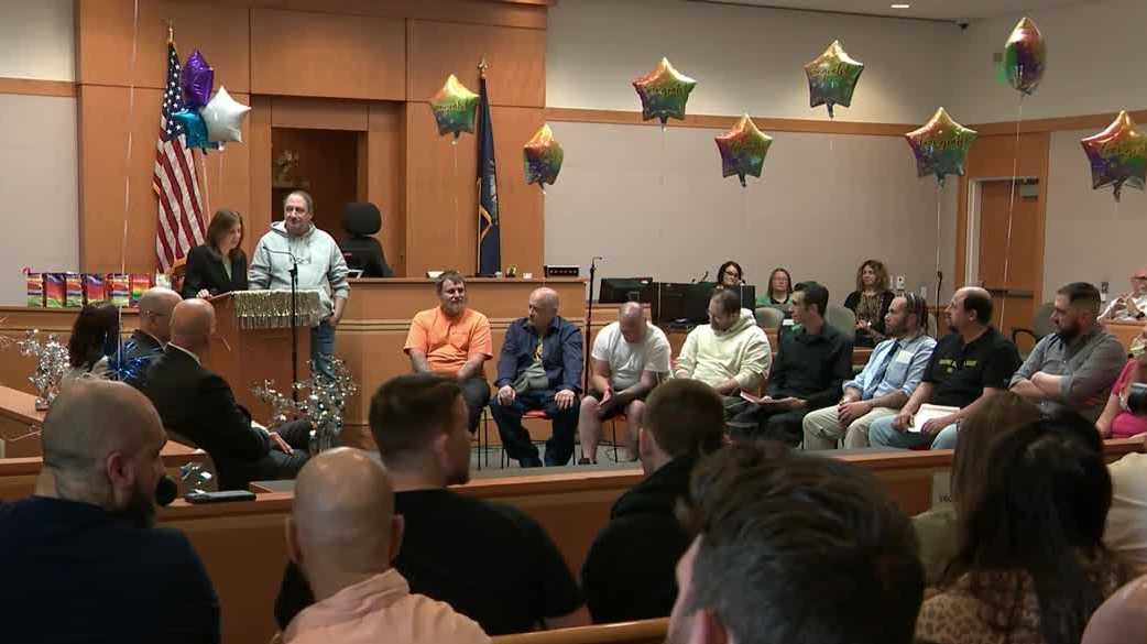 wp-header-logo-689png • Punkin's Patch A courtroom or council chamber with a raised bench, American flag, and people seated in a semicircle around a speaker at a podium adorned with garland; colorful balloons hang from the ceiling.