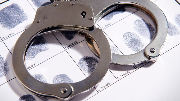 Metal handcuffs resting on a fingerprint chart used in forensic analysis.