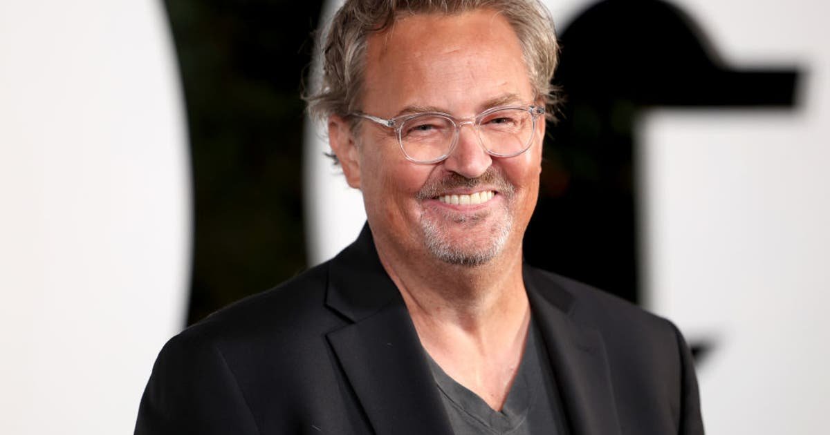 Smiling man with gray hair and glasses wearing a dark blazer at a formal event.