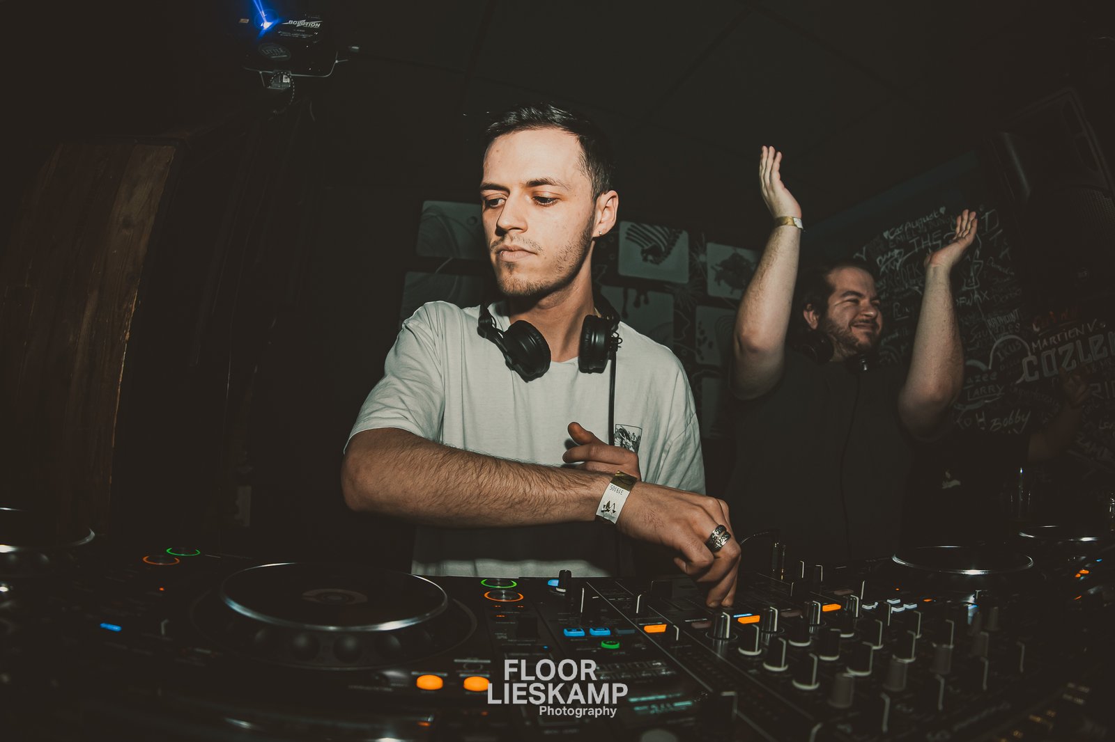 DJ wearing headphones at a mixing console in a dark club, hands moving as crowd raises arms in the background