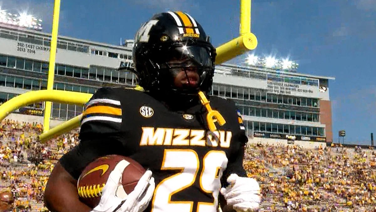 Missouri football player in a black jersey number 28 holding a football near the yellow goal post at a crowded stadium.