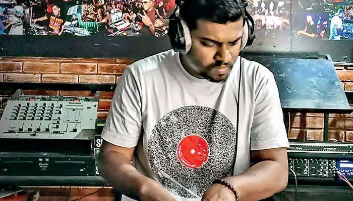 DJ wearing headphones, mixing on turntables and a mixer in a brick-walled venue.