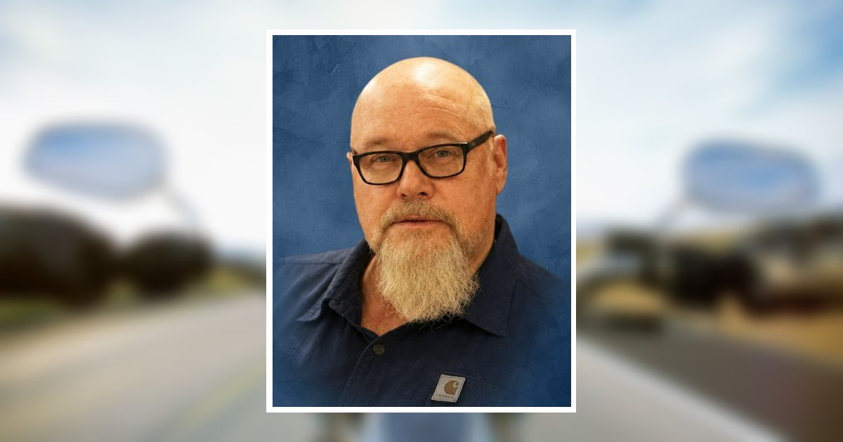 Portrait of a bald man with glasses and a blond goatee, wearing a dark shirt, against a blue backdrop.