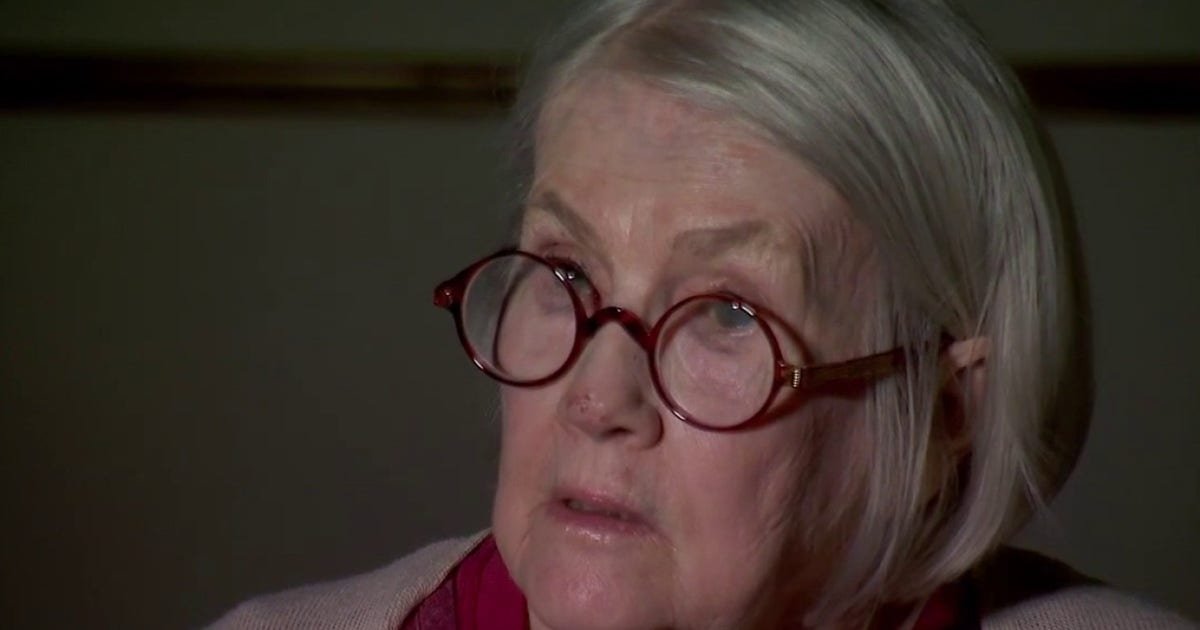 Close-up of an elderly woman with white hair and red round glasses.