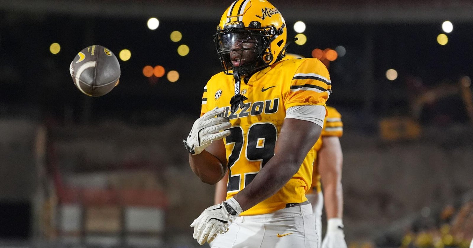 Missouri Tigers football player in yellow jersey (#29) on a night field watching a ball in midair near him.