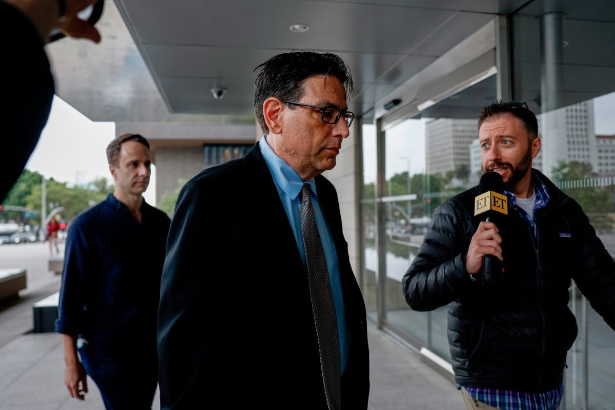 Man in a suit and glasses being interviewed outside a glass-front building by a reporter with an ET-branded microphone; another man stands in the background.
