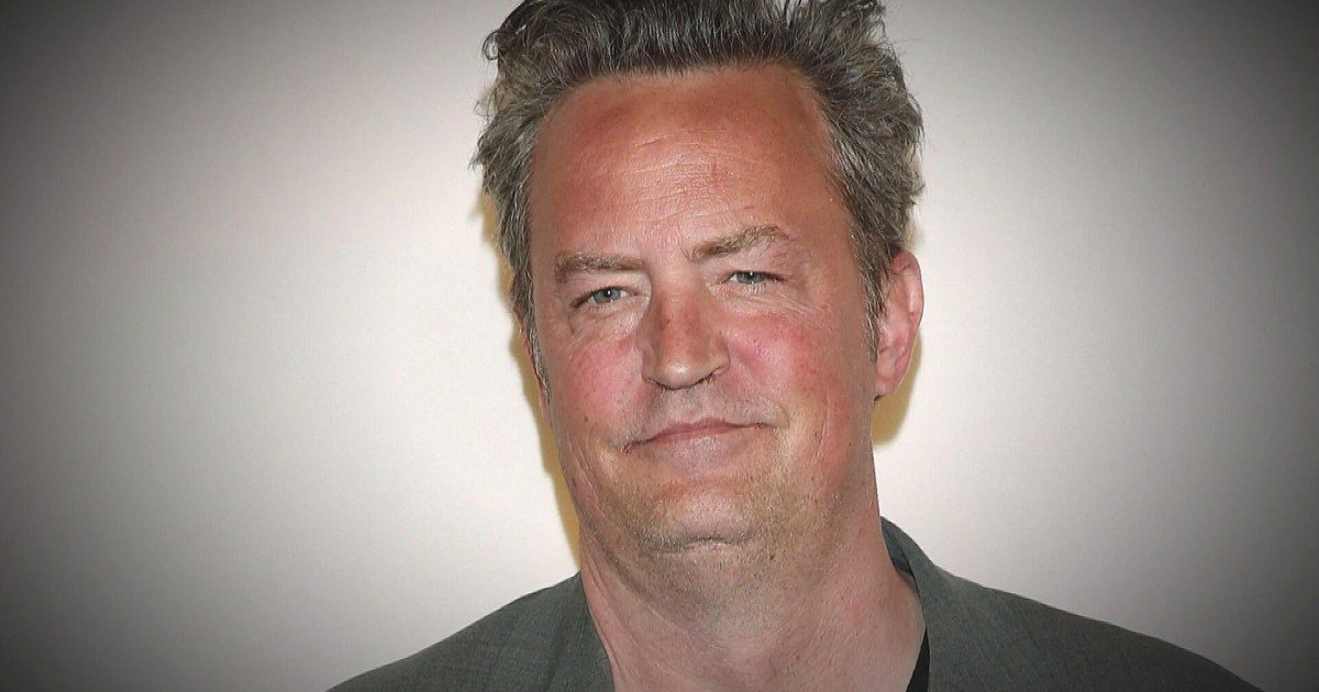 Portrait of a smiling middle-aged man with gray hair and a blazer against a neutral background.