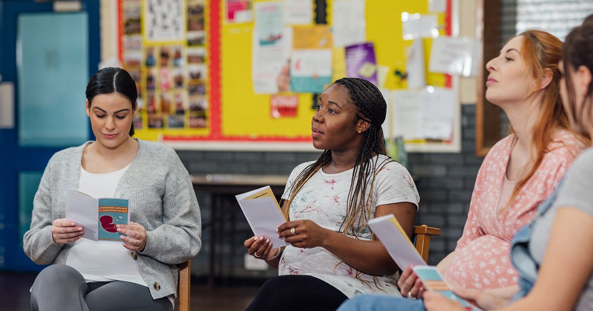 Group of diverse women seated in a circle, reading pamphlets during a workshop in a bright room.