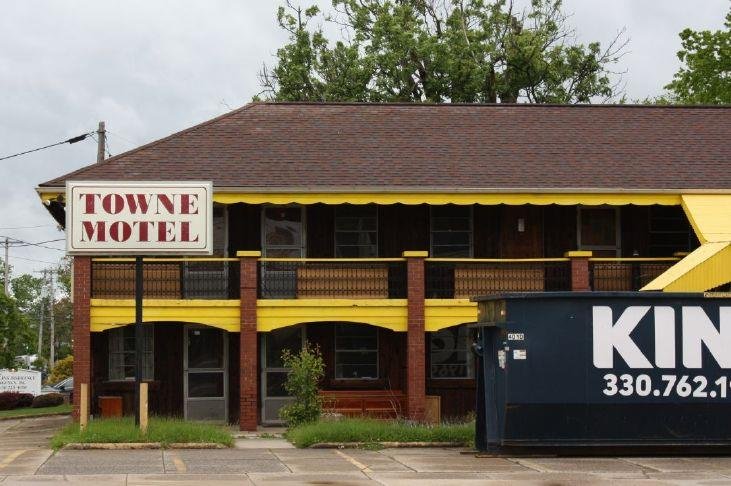 Front view of the Towne Motel: a two-story brick building with yellow awnings and a second-floor walkway, with a blue dumpster in the foreground on the right.