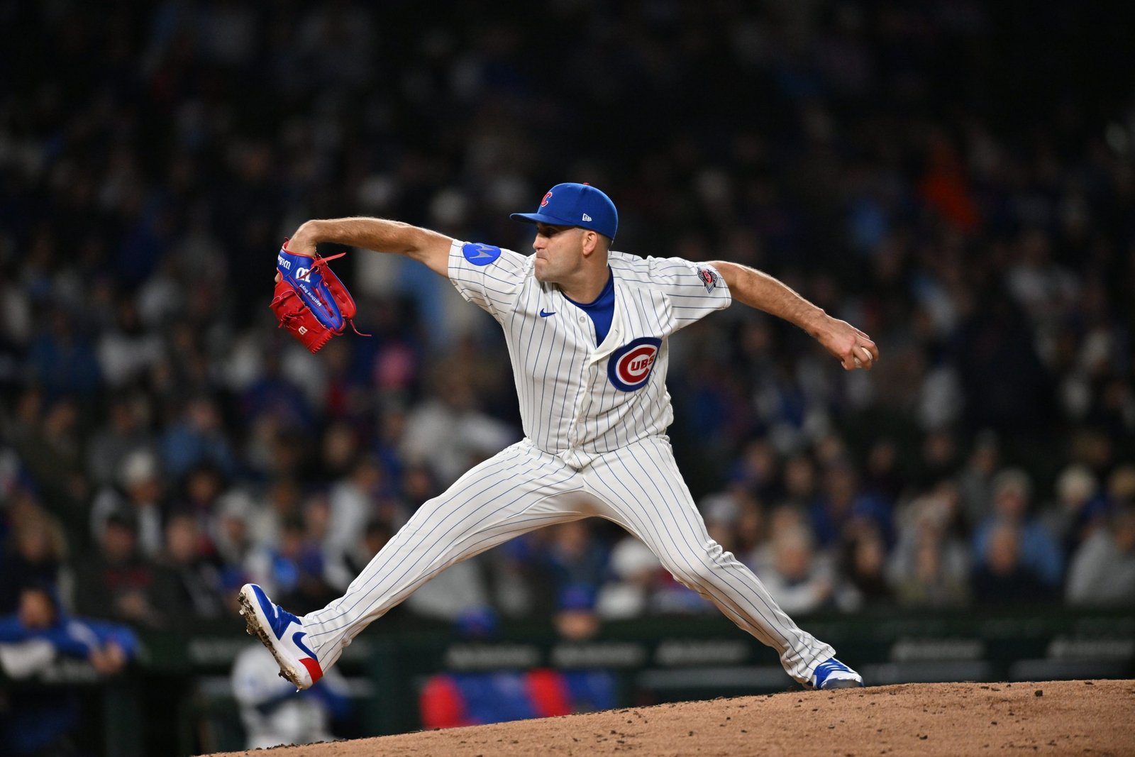 Chicago Cubs pitcher in pinstripe uniform delivering a pitch on the mound with a blurred crowd behind him.