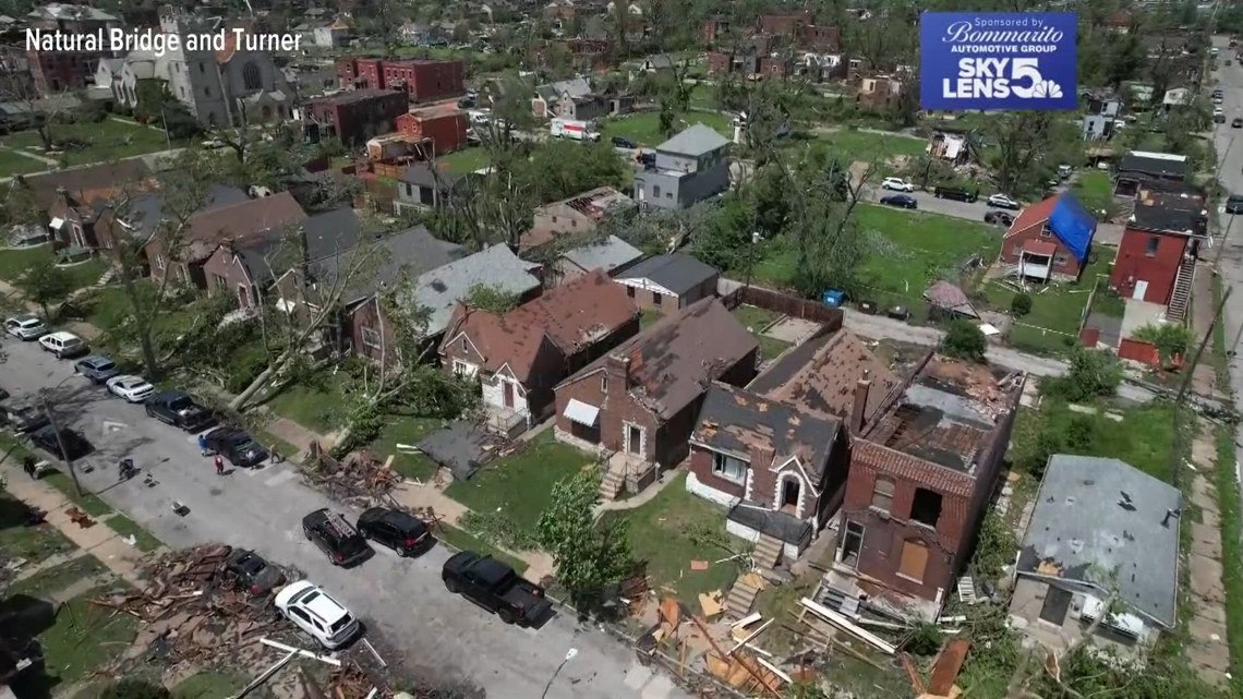 Aerial view of a residential neighborhood with damaged roofs, downed trees, and scattered debris from a recent storm.