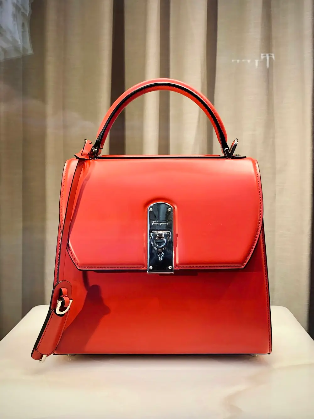 Red leather handbag with a silver-toned front clasp on a white display surface, top handle visible.