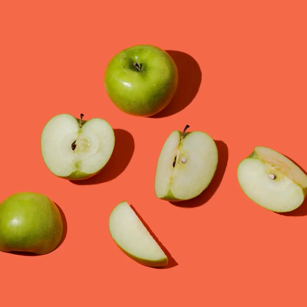 Several green apples and apple slices arranged on a bright orange background, showing the white flesh and seeds in the halves.